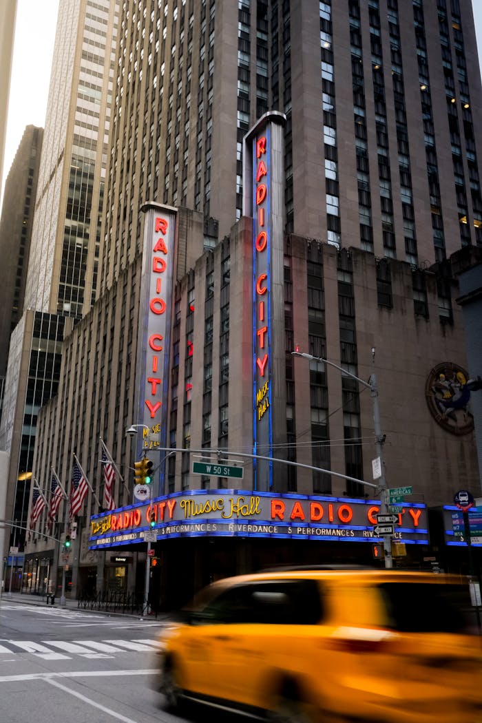 Colorful view of Radio City Music Hall with a yellow taxi in motion, capturing the essence of New York City.